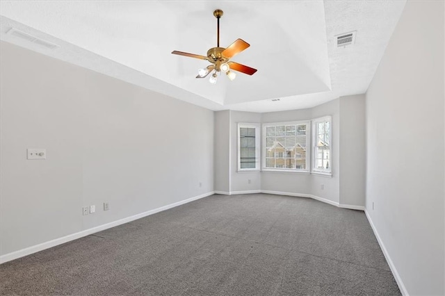 spare room featuring visible vents, a raised ceiling, baseboards, and dark colored carpet