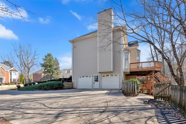 view of side of property featuring an attached garage, fence, stairs, a chimney, and driveway