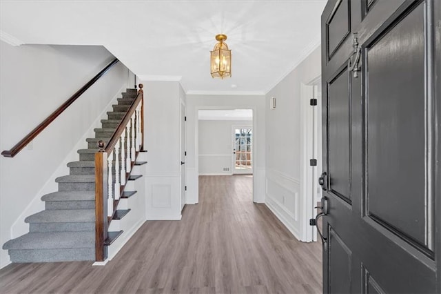 entrance foyer with a wainscoted wall, light wood-style flooring, stairway, crown molding, and a decorative wall