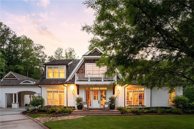 back of property with a balcony, a lawn, and brick siding