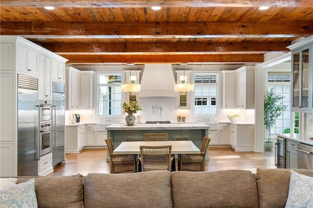 kitchen featuring custom exhaust hood, wood ceiling, light wood-style flooring, appliances with stainless steel finishes, and glass insert cabinets