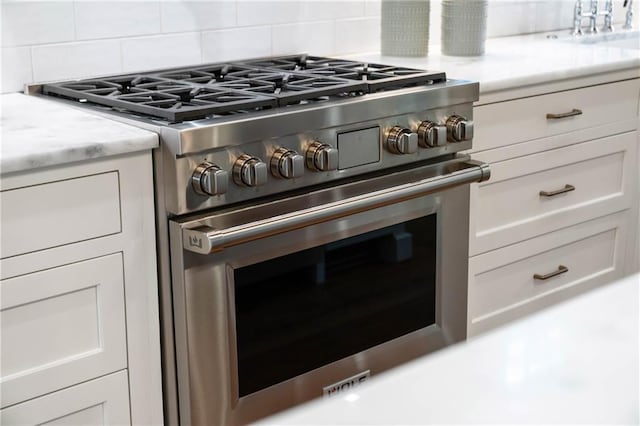 kitchen view of stainless steel range, a sink, decorative backsplash, and white cabinets