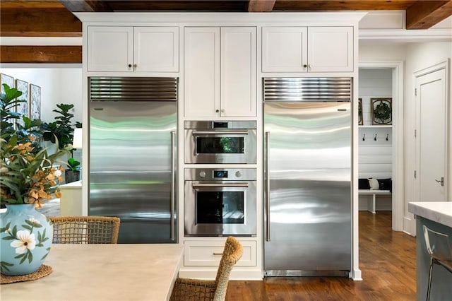 kitchen featuring appliances with stainless steel finishes, light countertops, dark wood finished floors, beam ceiling, and white cabinetry