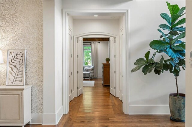 hall featuring wallpapered walls, wood finished floors, and arched walkways