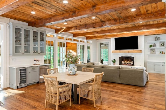 dining area featuring beverage cooler, wood ceiling, light wood-style flooring, a bar, and a fireplace