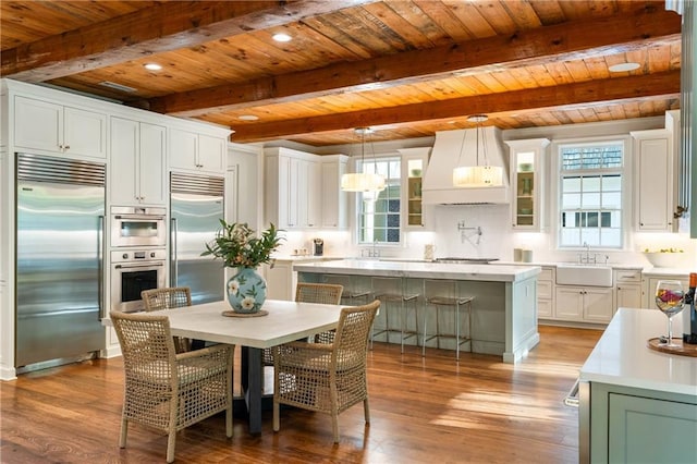 kitchen with appliances with stainless steel finishes, custom range hood, wood ceiling, a center island, and wood finished floors