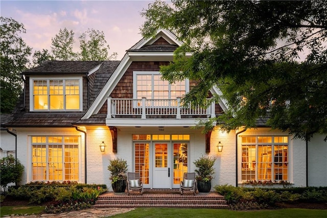 back of property at dusk featuring a balcony, a porch, and brick siding