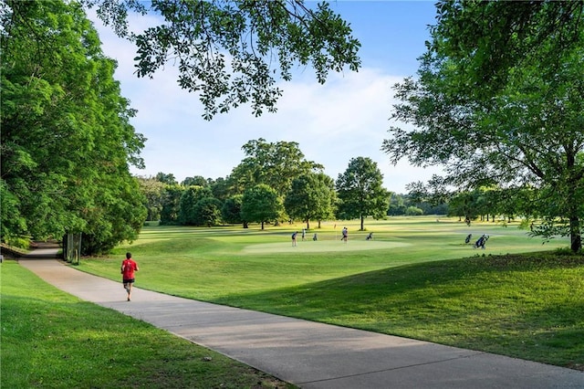 view of property's community featuring golf course view, a lawn, and view of wooded area