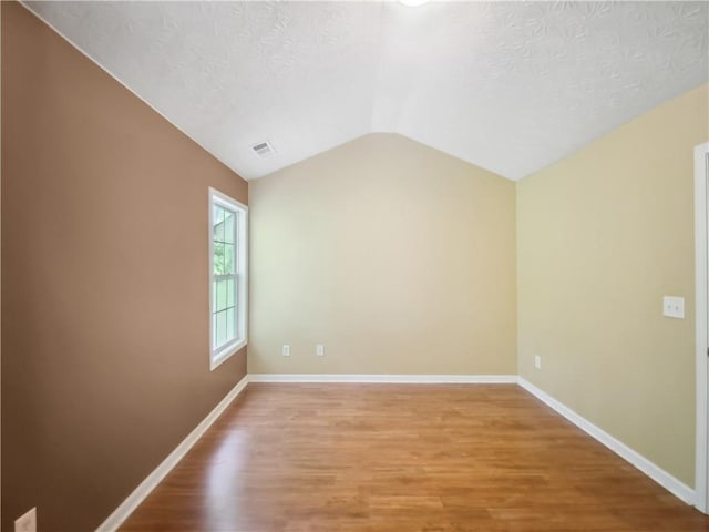 spare room featuring wood-type flooring, a textured ceiling, and lofted ceiling