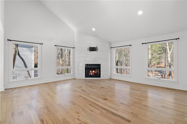 unfurnished living room featuring light wood-type flooring, a wealth of natural light, a tiled fireplace, and high vaulted ceiling