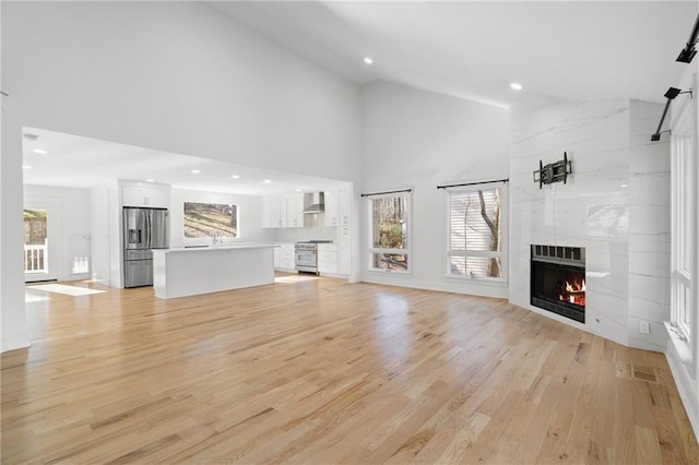 unfurnished living room featuring high vaulted ceiling, light hardwood / wood-style flooring, a healthy amount of sunlight, and a fireplace