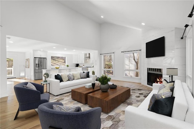 living room with high vaulted ceiling, light hardwood / wood-style floors, and a high end fireplace