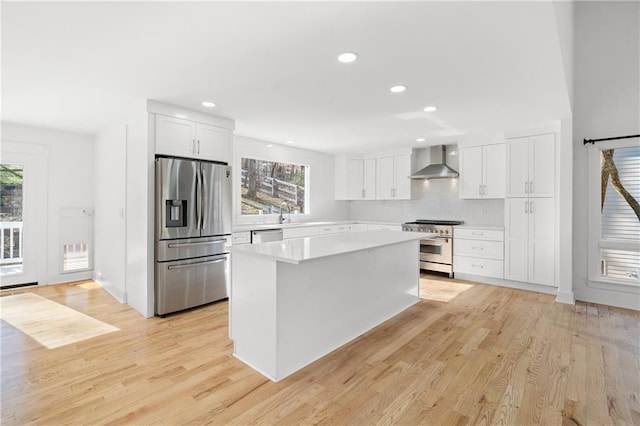 kitchen featuring a wealth of natural light, appliances with stainless steel finishes, white cabinetry, and wall chimney range hood