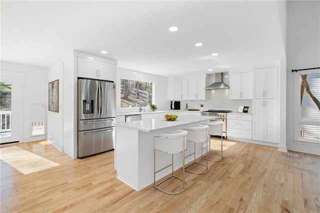 kitchen with white cabinets, appliances with stainless steel finishes, a center island, wall chimney range hood, and a kitchen breakfast bar