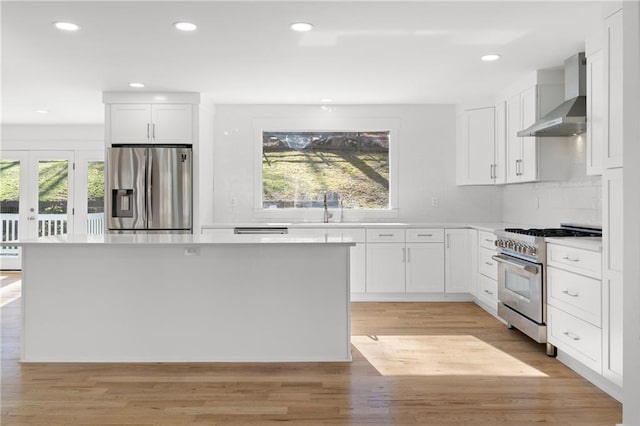 kitchen with appliances with stainless steel finishes, light hardwood / wood-style flooring, white cabinets, and wall chimney range hood