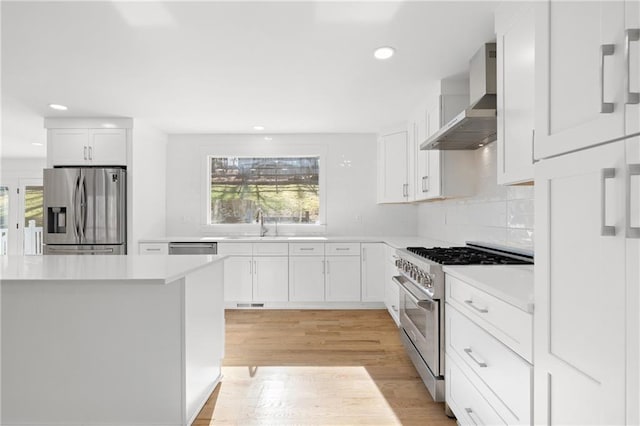 kitchen with white cabinets, wall chimney range hood, a healthy amount of sunlight, and stainless steel appliances