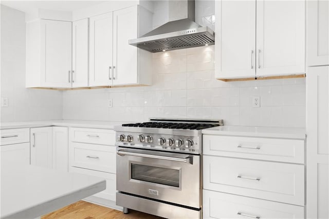 kitchen featuring white cabinets, wall chimney exhaust hood, decorative backsplash, high end stove, and light hardwood / wood-style flooring