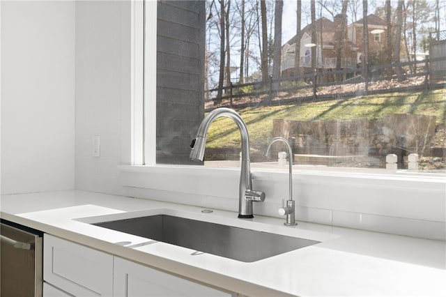 kitchen with stainless steel dishwasher, sink, and white cabinetry