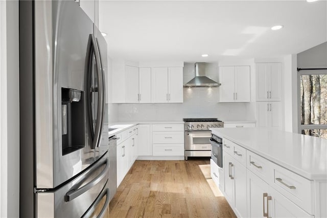 kitchen with white cabinets, wall chimney exhaust hood, stainless steel appliances, and light hardwood / wood-style flooring