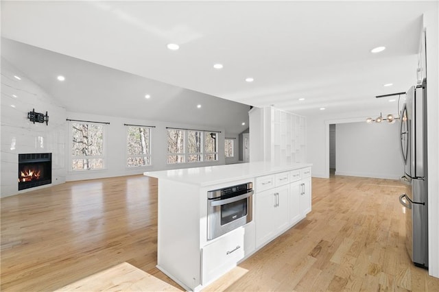 kitchen with white cabinetry, stainless steel appliances, a kitchen island, light hardwood / wood-style flooring, and a tile fireplace