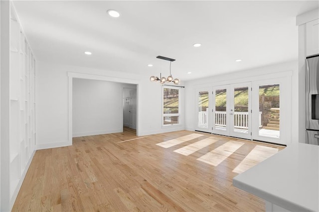 unfurnished living room with light wood-type flooring, french doors, and a notable chandelier