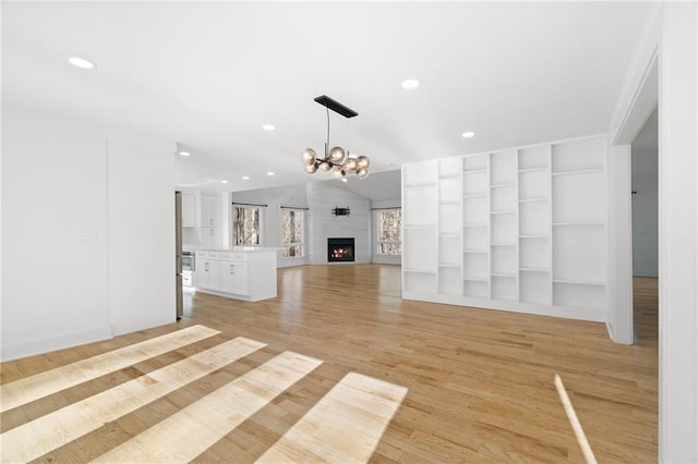 unfurnished living room with lofted ceiling, a fireplace, light hardwood / wood-style floors, an inviting chandelier, and built in features