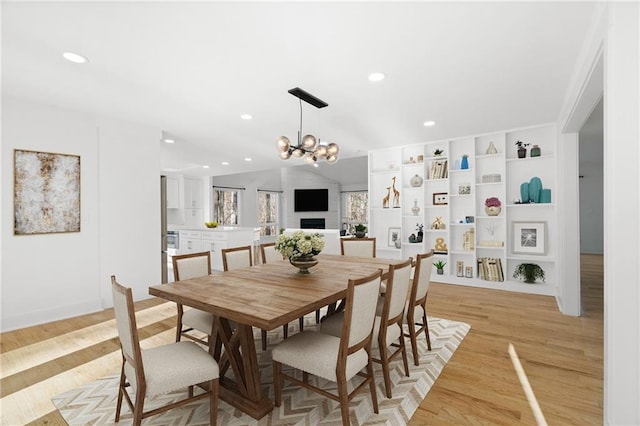 dining space featuring light hardwood / wood-style floors, vaulted ceiling, built in features, and an inviting chandelier