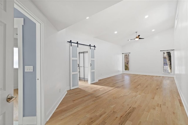 unfurnished living room featuring vaulted ceiling, ceiling fan, light hardwood / wood-style floors, and a barn door