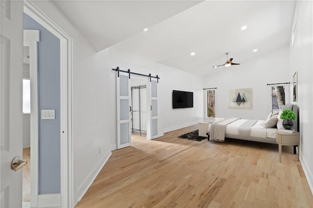 bedroom featuring light hardwood / wood-style floors, ceiling fan, a barn door, and vaulted ceiling