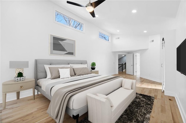 bedroom with ceiling fan, light hardwood / wood-style floors, and a towering ceiling