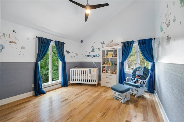 bedroom featuring ceiling fan, a nursery area, multiple windows, and hardwood / wood-style flooring