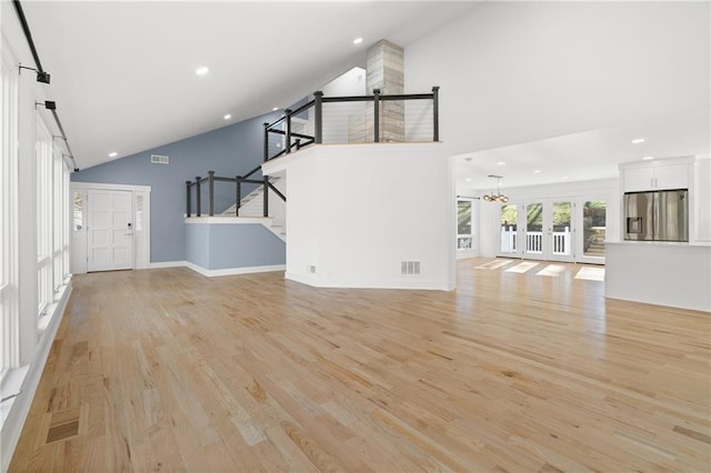 unfurnished living room with a notable chandelier, light hardwood / wood-style flooring, french doors, and high vaulted ceiling