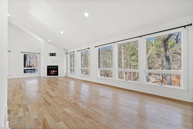 unfurnished living room featuring light wood-type flooring, a tile fireplace, and high vaulted ceiling