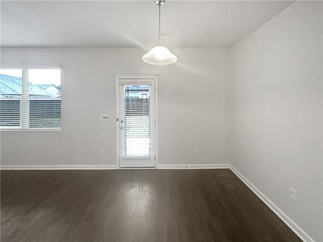 empty room featuring baseboards, dark wood finished floors, and a wealth of natural light