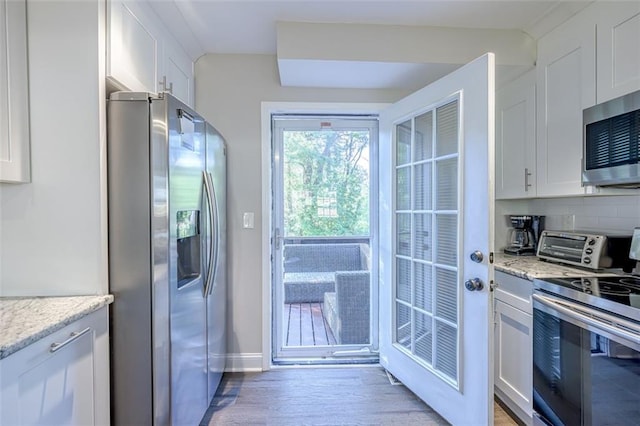 kitchen with white cabinetry, light stone countertops, light wood-type flooring, and appliances with stainless steel finishes