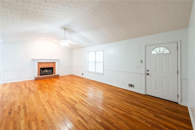 unfurnished living room with hardwood / wood-style floors, ceiling fan, a fireplace, a textured ceiling, and lofted ceiling