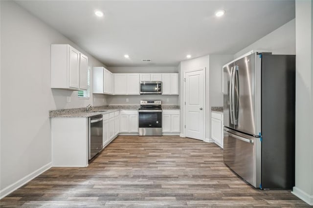 kitchen with white cabinetry, light stone countertops, stainless steel appliances, wood-type flooring, and sink