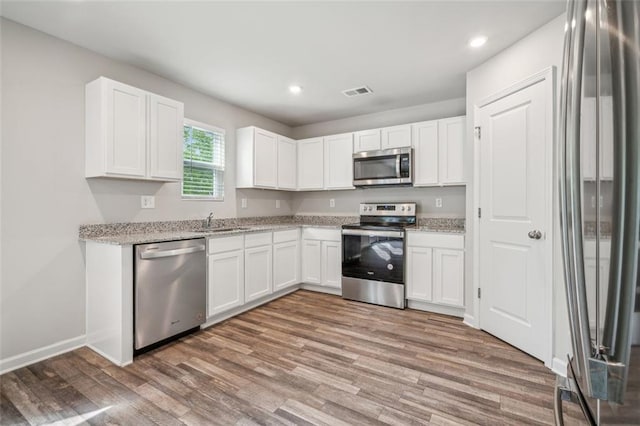 kitchen featuring appliances with stainless steel finishes, hardwood / wood-style flooring, white cabinets, and light stone countertops