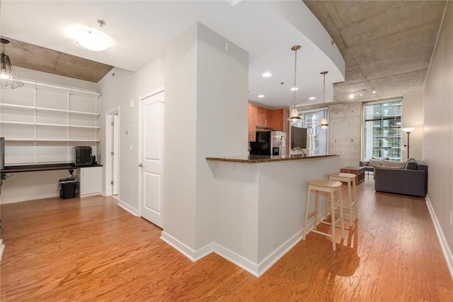 kitchen featuring baseboards, stainless steel fridge with ice dispenser, light wood-style flooring, a kitchen breakfast bar, and open floor plan