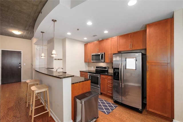 kitchen featuring a breakfast bar, light wood-style floors, appliances with stainless steel finishes, brown cabinets, and dark stone countertops