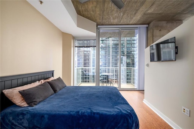 bedroom featuring ceiling fan, wood finished floors, baseboards, access to outside, and floor to ceiling windows