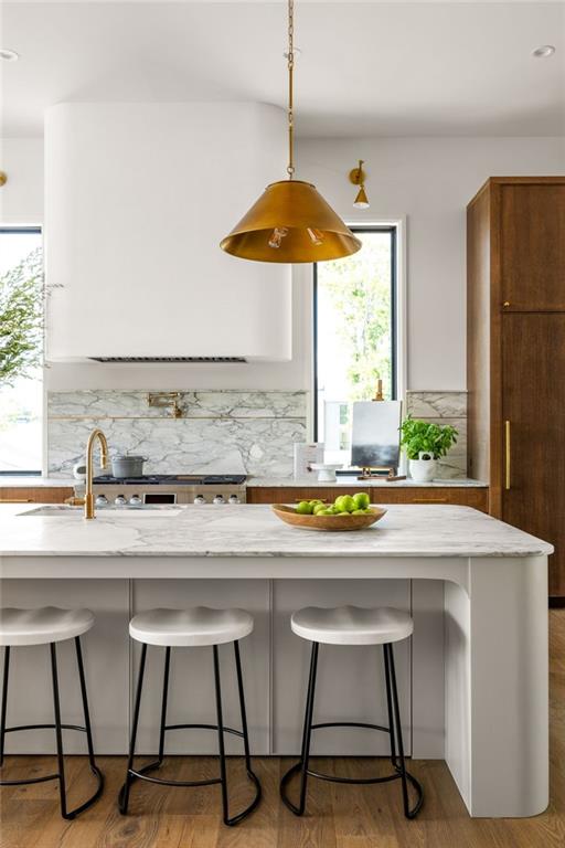 kitchen featuring tasteful backsplash, high end stove, a center island with sink, hanging light fixtures, and a breakfast bar area