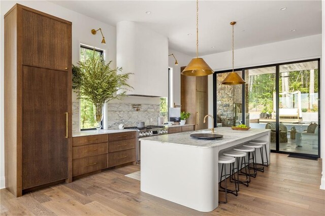 kitchen featuring hanging light fixtures, light stone counters, hardwood / wood-style floors, an island with sink, and range with two ovens