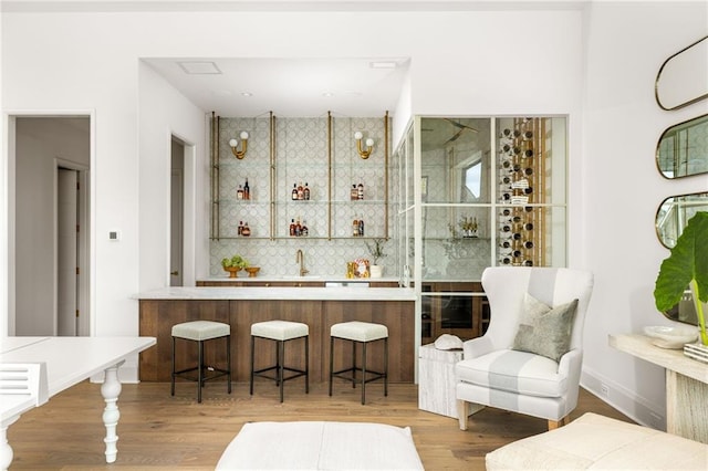 bar featuring decorative backsplash, light hardwood / wood-style floors, and sink