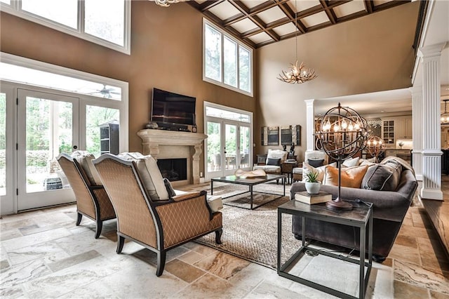 living area with french doors, decorative columns, stone tile flooring, a chandelier, and a high ceiling