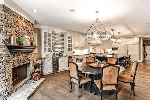 dining area featuring a fireplace, beverage cooler, a chandelier, ornamental molding, and recessed lighting