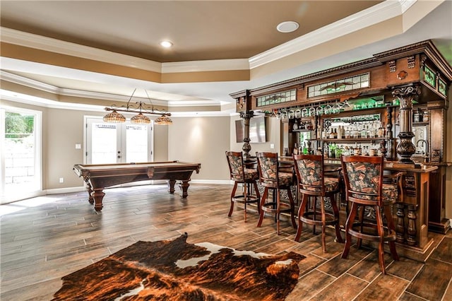 bar with a community bar, a tray ceiling, ornamental molding, and wood finished floors