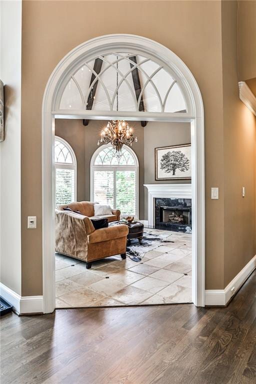 living room featuring a high ceiling, a premium fireplace, a chandelier, baseboards, and wood finished floors