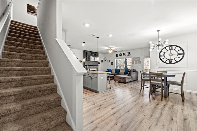 stairs with recessed lighting, baseboards, wood finished floors, and ceiling fan with notable chandelier