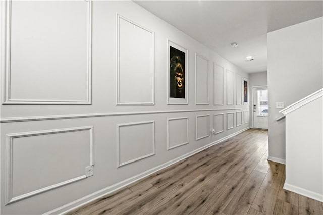 hall featuring a decorative wall, baseboards, and wood finished floors